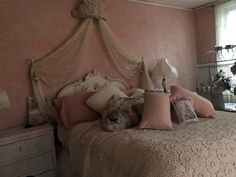 a bedroom with pink walls and white bedding, two lamps on nightstands and a birdcage hanging from the ceiling