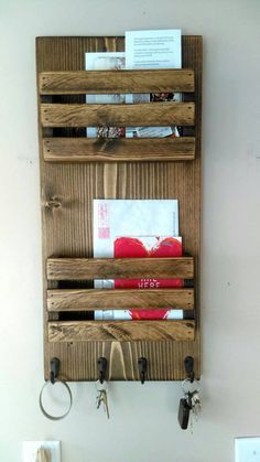 a wooden wall mounted shelf with key hooks and mail holders on the bottom, holding several items