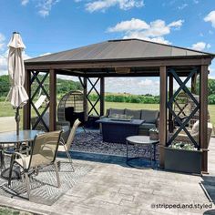 a gazebo with chairs, tables and umbrellas on the patio area in front of an open field