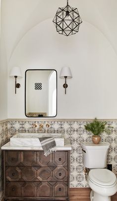 a white toilet sitting next to a wooden dresser in a bathroom under a large mirror