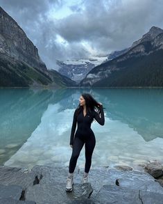 a woman standing on top of a rock next to a lake