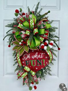 a christmas wreath hanging on the front door with green and red ribbons, white pom - poms and an ornament that says oh what fun