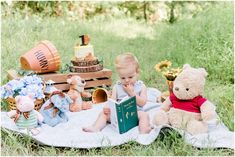 a baby sitting on a blanket reading a book with stuffed animals around him and other toys in the background