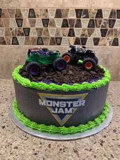 a monster jam cake with green frosting and monster trucks on the top is sitting on a counter