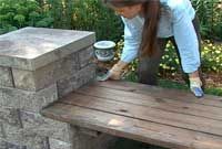 a woman bending over to put something in a bucket on top of a wooden bench