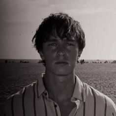 a man standing in front of a body of water with boats on the ocean behind him