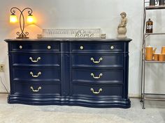 a large blue dresser with gold handles in a room next to a shelf and lamp