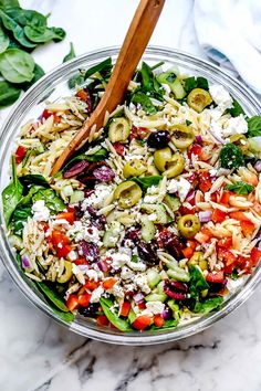 a salad in a glass bowl with olives, feta cheese and spinach