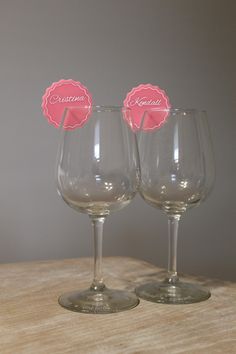 two wine glasses sitting on top of a wooden table next to each other with pink tags in them