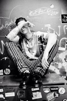 a young man sitting on top of a suitcase covered in stickers and graffiti, with his hands behind his head