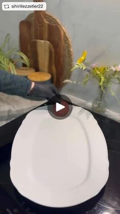 a white plate sitting on top of a counter next to a vase filled with flowers