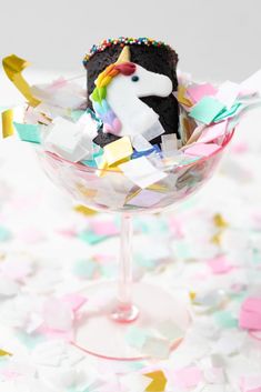 a unicorn cake in a wine glass surrounded by confetti and sprinkles