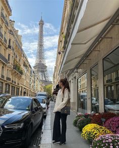 a person is standing in front of the eiffel tower with cars parked on the sidewalk