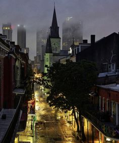 a city street at night with rain on the ground and tall buildings in the background