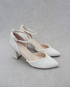 a pair of white high heeled shoes sitting on top of a gray cloth covered floor