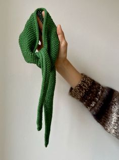 a person's hand holding up a green knitted scarf in front of a white wall