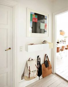 two purses are hanging on the wall in front of an open door with a table and chairs