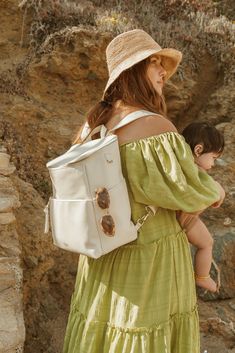 a woman in a green dress carrying a white bag and a child wearing a straw hat