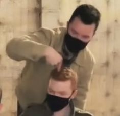 a man is cutting another mans hair with a black mask