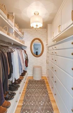 an organized closet with white drawers and lots of clothes hanging on the shelves, along with a large round mirror