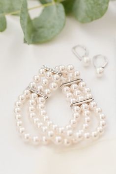 three pearl bracelets and earrings on a white table with green leaves in the background