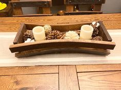 a wooden tray with two candles and pine cones in it on top of a table