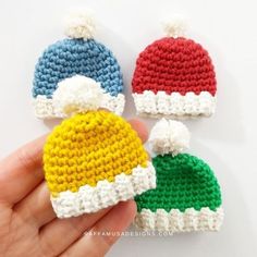 three crocheted hats are being held up by someone's hand on a white surface