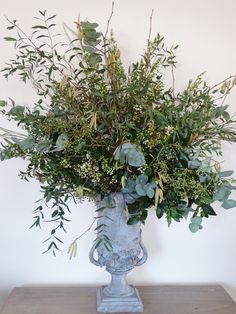 a vase filled with lots of greenery on top of a wooden table