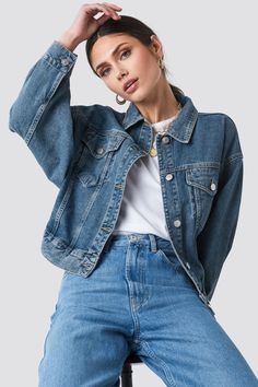 a woman wearing a denim jacket and jeans sitting on a stool with her hands behind her head