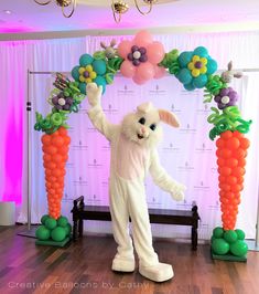 a person dressed as a bunny standing in front of some carrots and balloon decorations