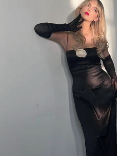 a woman in a black dress leaning against a wall