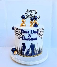 a white and blue birthday cake with two people on it's side, surrounded by gold balls