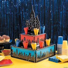 a table topped with cakes and cupcakes covered in frosting next to blue curtains