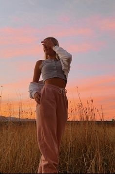 a woman standing in tall grass at sunset