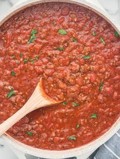 a wooden spoon in a pot filled with chili sauce and garnished with parsley