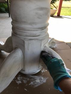 a person is painting the base of a white fire hydrant with blue gloves on