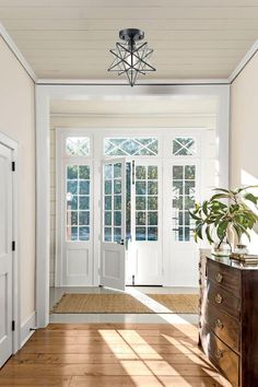 an empty hallway with wooden floors and white walls, leading to the front door that has french doors on both sides