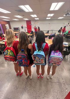 three girls with backpacks standing in a classroom