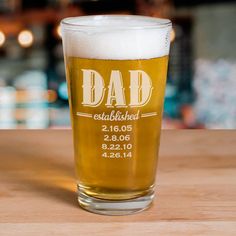 a beer glass sitting on top of a wooden table with the words dad attached to it