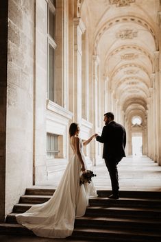 a bride and groom standing on the steps of an old building holding hands with each other