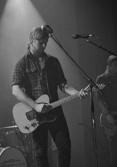 two men are playing guitars and singing into microphones in a black and white photo