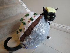 a black cat wearing a plastic bag with food on it's head and wrapped in foil