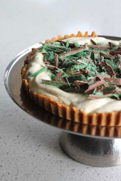 there is a pie with green and white frosting on the top, sitting on a silver platter