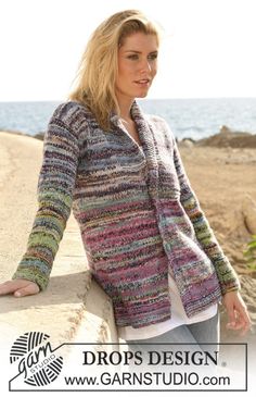 a woman leaning on a wall next to the ocean wearing a colorful sweater and jeans