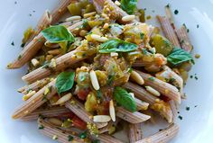 pasta with pesto, pine nuts and basil on a white plate topped with parsley