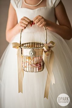 a woman in a white dress is holding a birdcage with ribbons on it