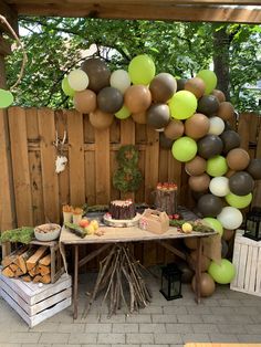 a table topped with lots of balloons next to a wooden fence covered in wood logs