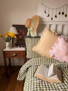 an open book is sitting on a bed with gingham comforter and pillows