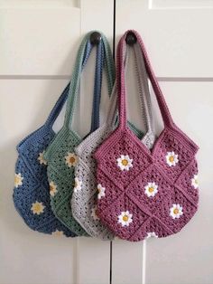 three crocheted purses hanging from hooks on a door with daisies in them