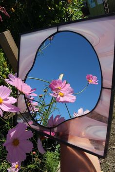 a hand holding a mirror with pink flowers in front of it and the reflection of a blue sky